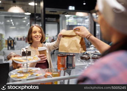 small business, takeaway food, people and service concept - happy female customer with coffee cup taking paper bag from man or barman at vegan cafe. woman taking paper bag from seller at cafe