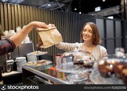 small business, takeaway food, people and service concept - happy female customer taking paper bag from man or barman at vegan cafe. woman taking paper bag from seller at cafe