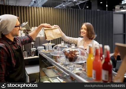small business, takeaway food, people and service concept - happy female customer taking paper bag from man or barman at vegan cafe. woman taking paper bag from seller at cafe. woman taking paper bag from seller at cafe
