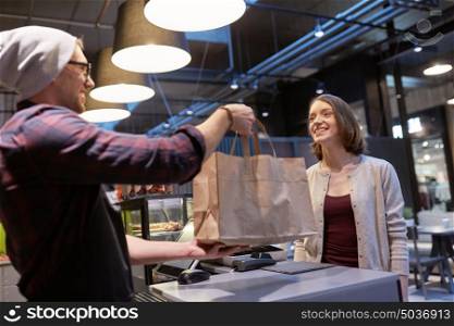 small business, takeaway food, people and service concept - man or seller giving paper bag to happy female customer at vegan cafe. seller giving paper bag to customer at vegan cafe