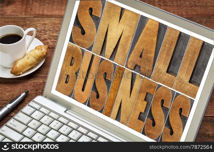 small business text in letterpress wood type printing blocks on a laptop with a cup of coffee