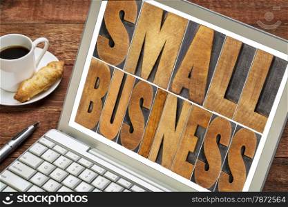 small business text in letterpress wood type printing blocks on a laptop with a cup of coffee