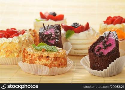 Small cakes with cream and berries on bamboo table cloth