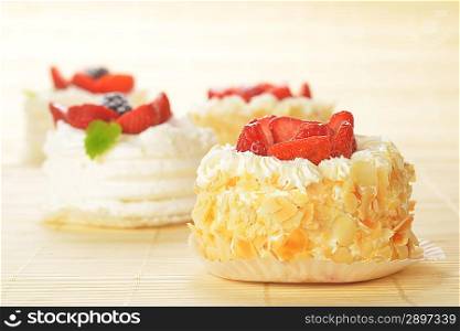 Small cakes with white icing and fruits on bamboo table cloth