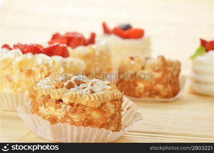 Small cakes with white icing and fruits on bamboo table cloth