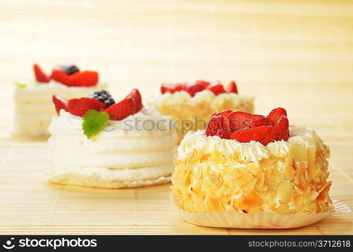 Small cakes with white icing and fruits on bamboo table cloth