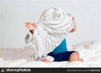 Small Caucasian boy playing under a striped blanket on white duvet bedding