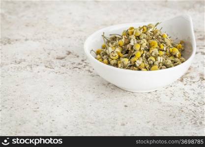 small ceramic bowl of dried chamomile flowers against a ceramic tile background with a copy space