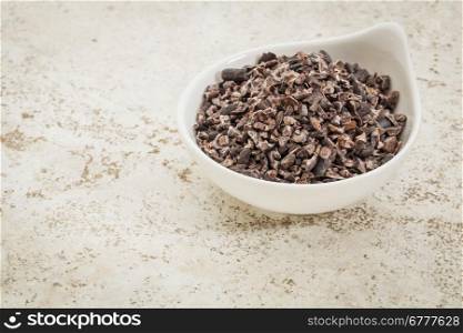 small ceramic bowl of raw cacao nibs against a ceramic tile background with a copy space