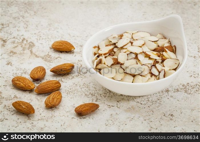 small ceramic bowl of sliced raw almonds against a ceramic tile background with a copy space