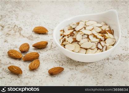 small ceramic bowl of sliced raw almonds against a ceramic tile background with a copy space