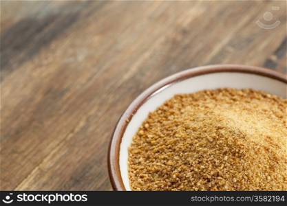 small ceramic bowl of unrefined coconut palm sugar against an out of focus wood background - copy space