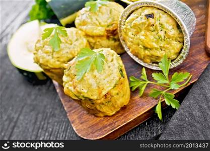 Small cheese and zucchini muffins with herbs, parsley, thyme, knife and a towel on the background of dark wooden board