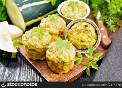 Small cheese and zucchini muffins with herbs, parsley, thyme, knife and a napkin on black wooden board background