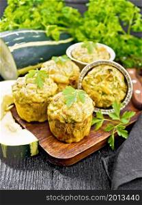 Small cheese and zucchini muffins with herbs, parsley, thyme, knife and napkin on the background of a dark wooden board