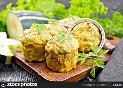 Small cheese and zucchini muffins with herbs, parsley, thyme, knife and towel on a wooden board background