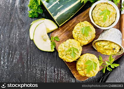 Small cheese and zucchini muffins with herbs, parsley, thyme, knife and towel on a dark wooden board background from above