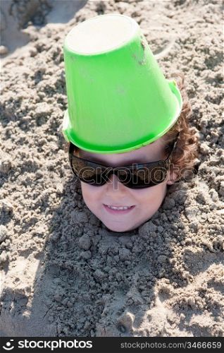 Small child buried in the sand of the beach with sunglasses