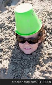 Small child buried in the sand of the beach with sunglasses