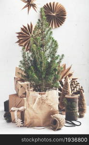 Small Christmas tree in a pot wrapped in paper, undecorated, gifts in kraft paper and decorations on brick wall background, Zero waste eco Christmas and New Year concept. Zero waste eco Christmas and New Year concept