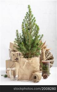 Small Christmas tree in a pot wrapped in paper, undecorated, gifts in kraft paper and decorations on brick wall background, Zero waste eco Christmas and New Year concept