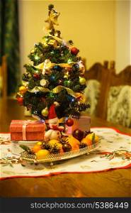 Small Christmas tree with decorations, gifts and citrus on the table
