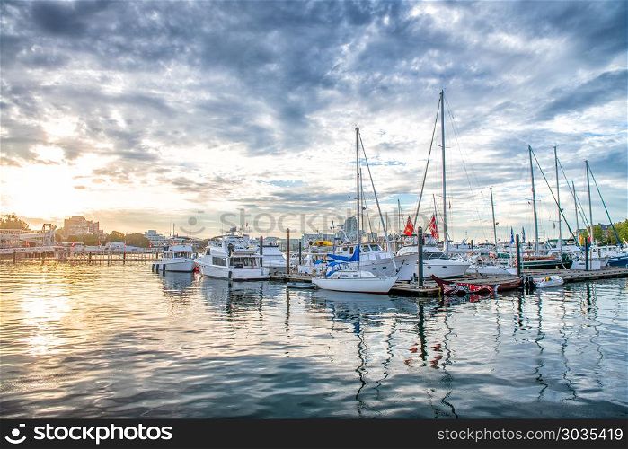 Small city port with docked boats at sunset against cloudy sky.. Small city port with docked boats at sunset against cloudy sky