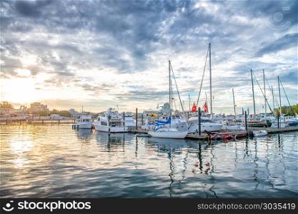 Small city port with docked boats at sunset against cloudy sky.. Small city port with docked boats at sunset against cloudy sky