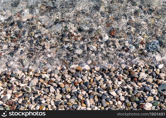 Small color wet pebbles on sea shore. Close-up view from above. Texture, wallpaper, background.