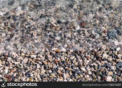 Small color wet pebbles on sea shore. Close-up view from above. Texture, wallpaper, background.