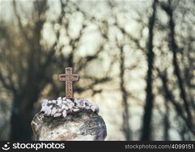 Small cross made of bronze and trees in background