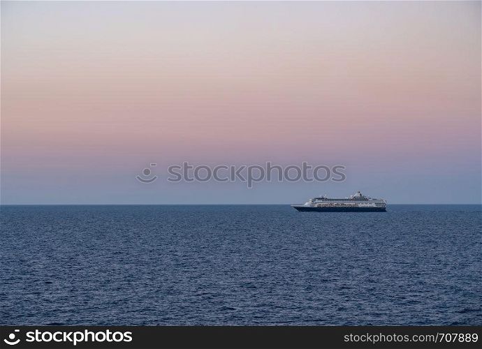 Small cruise liner sailing across the ocean as dawn starts to light the sky. Cruise ship sailing the seas at sunrise or dawn