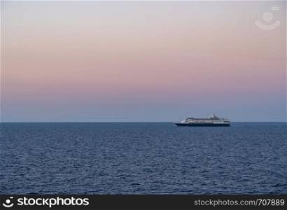Small cruise liner sailing across the ocean as dawn starts to light the sky. Cruise ship sailing the seas at sunrise or dawn