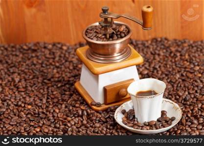 small cup of coffee and roasted coffee beans with retro copper manual mill and wooden wall
