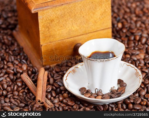 small cup of coffee and roasted coffee beans with retro wood manual mill, cinnamon close up