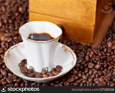 small cup of coffee and roasted coffee beans with retro wood manual mill close up