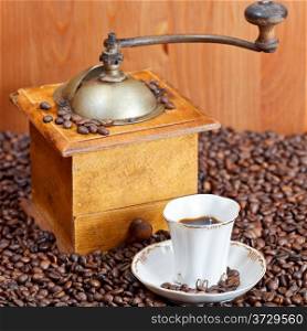 small cup of coffee and roasted coffee beans with retro wooden manual grinder and wood wall