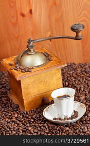 small cup of coffee and roasted coffee beans with retro wooden manual mill and wood wall