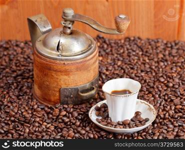 small cup of coffee and roasted coffee beans with vintage manual mill