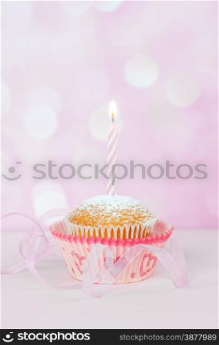 Small cupcakes with a one burning striped candle on a pink background