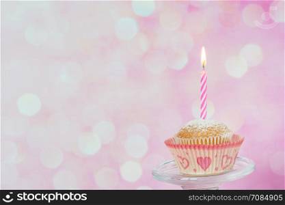 Small cupcakes with a one burning striped candle on a pink background