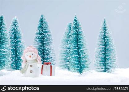Small cute snowman with gift in forest in snow cute Christmas card design. Snowman and gift