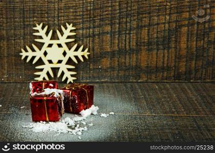 Small decorative gifts sprinkled with snow, two wooden snowflakes as a Christmas decoration on the wooden background. Horizontal view.