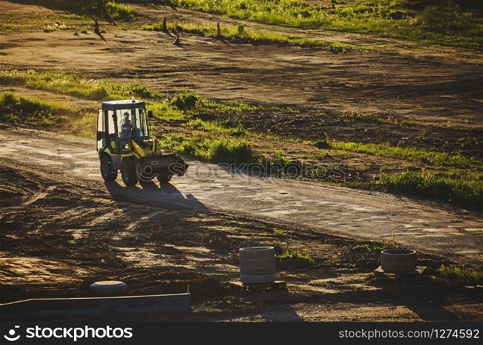 Small excavator car moving on a dusty road through construction place in sunset light