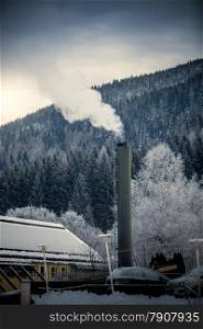 Small factory with steaming pipe in Alps at snowy day