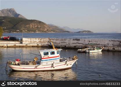 small fishing boats in harbor of agios nicolaos on greek peloponnese with sea and mountains in the background on sunny evening in april