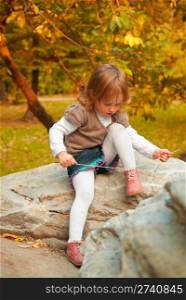 Small girl (3 years) tying shoelace in the autumn park at the evening