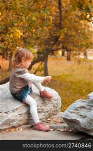 Small girl (3 years) tying shoelaces at the evening in the autumn park