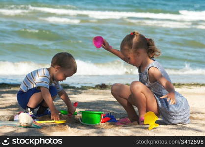 Small girl and boy play with sand near sea