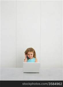 Small girl by desk using cell phone and laptop